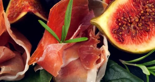 Figues, jamon et feuilles d'épinard sur une planche de service en pierre noire. Set de snacks