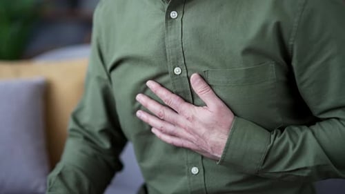 Close-up of male hands holding chest while suffering from heart attack at home. Mature man in shirt