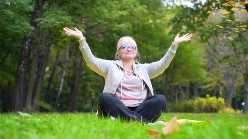 Portrait senior retired woman exercising on a mat on lawn a park Old female does yoga practice lotus