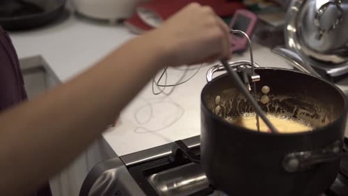 A young girl stirs a caramel mix heating up on the stove while baking millionaire shortbread cookies
