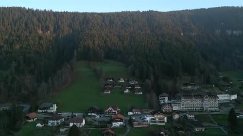 Drone Flies Away From Village Curvy Road Houses on Green Hill with Trees Interlaken Switzerland