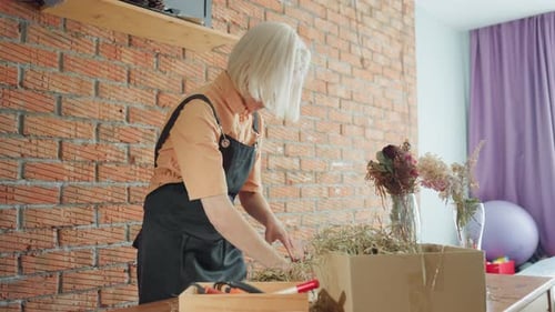 Woman crafting wreath at table in brightly lit room