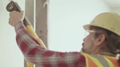 Senior construction worker cuts through partition wall in vacant office space Canada