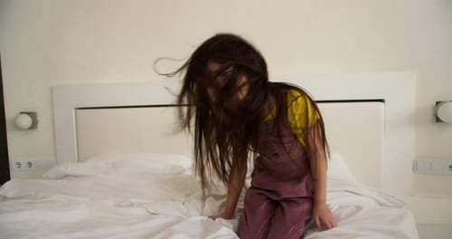 Girl Jumps on Bed Wearing Headphones