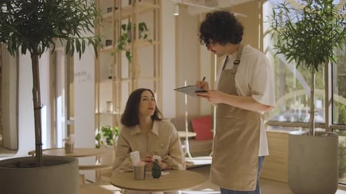 A Waiter Takes an Order From a Girl Who is Sitting at a Table in a Cafe A Beautiful Girl in a Good