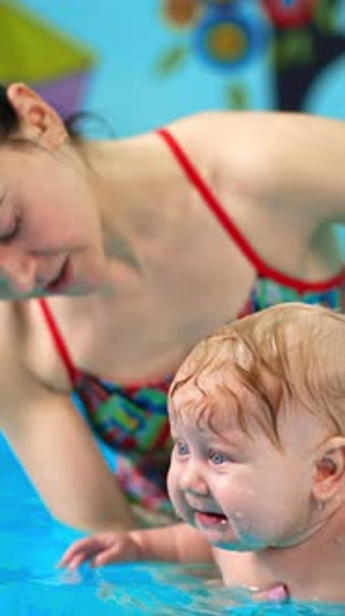 Caucasian woman holding a baby in the pool on her palm. Infant child is taught to swim.