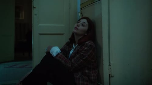 Worried Woman Sitting Against Wall in Dark Hallway