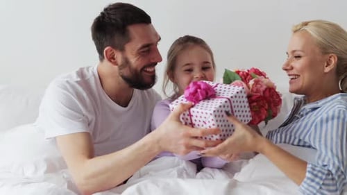 Happy family in bed presents mother with gifts