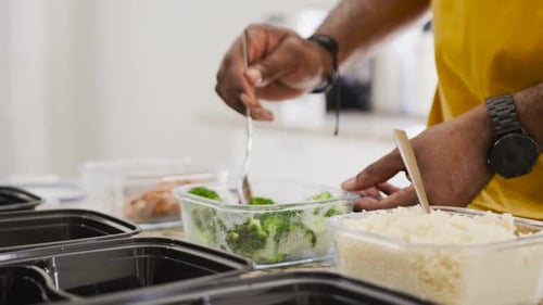 Après la cuisson, un homme en chemise jaune met du brocoli dans des plateaux de préparation des repas sur le comptoir, espace de copie