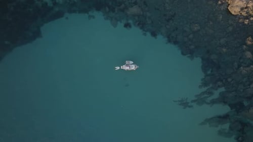 Drone top down rising above boat with dinghy and raft in turquoise green sandy water