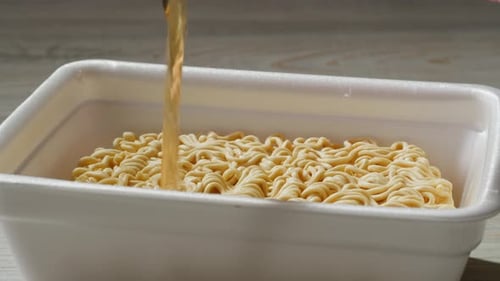 Broth Being Poured Over Dry Noodles in Container