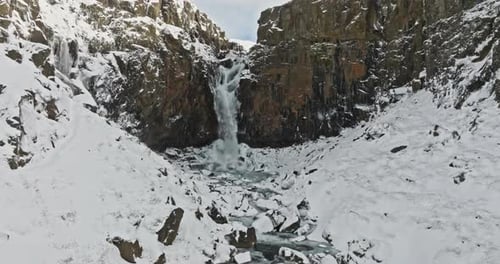 Drohne nähert sich einem verschneiten Berg mit Wasserfall