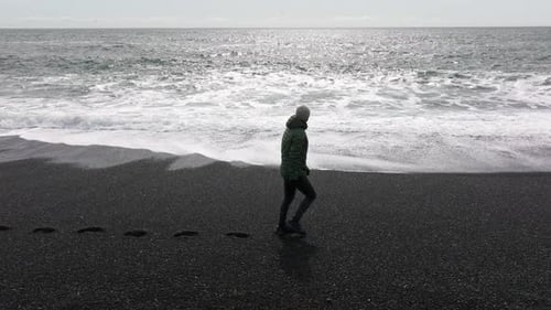 Man Walking Along Black Sand Beach with Sea