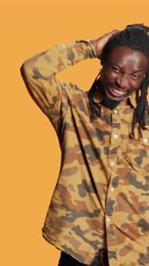Man with Braids Poses Smiling in Front of Orange