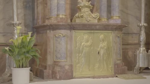 Um crucifixo está acima de um tabernáculo em um altar barroco, dois castiçais e flores
