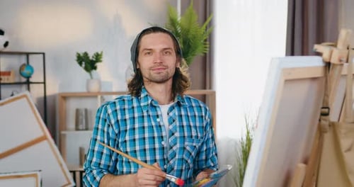 Portrait of man artist which looking into camera during creating beautiful picture in own studio