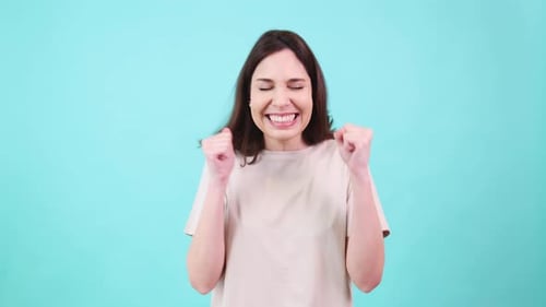 Excited Woman Celebrating with Fists in the Air on Turquoise Background
