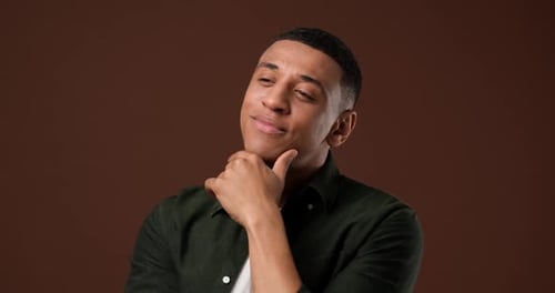Closeup Portrait of Pensive Young African American Man Smiling and Looking Over Brown Studio