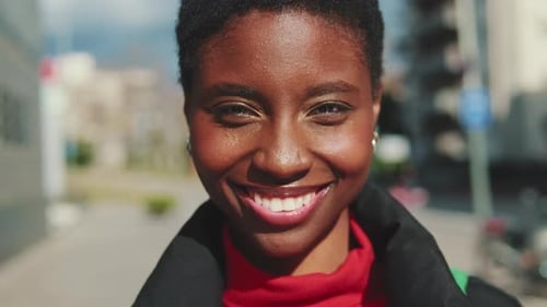 Close up, young smiling woman standing a city street looking at camera