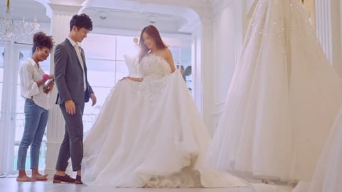Asian beautiful bride trying on wedding gown with her fiance in studio.