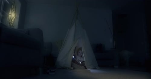 Child Reading Book in Dark Tent Inside Home