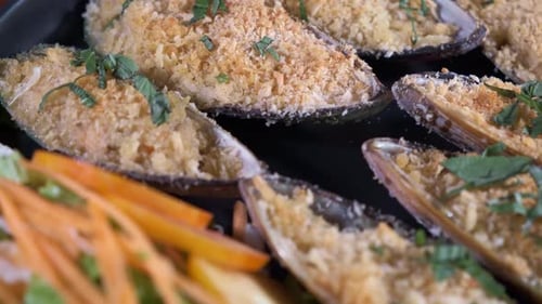 Authentic Freshly oven cooked Mussels Spinning on a Black Plate with Sliced Vegetables Close Up Shot