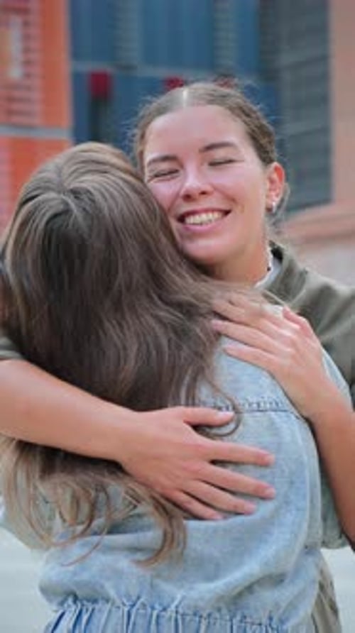Two Young Women Embracing and Smiling in City