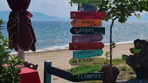 sea with sandy beach in greece and signs showing directions and distance to different cities. Tilt u