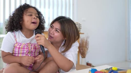 Child and Woman Singing with a Microphone Indoors