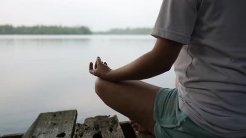Woman Meditating While Seating on a Wooden Pier with Lake in the Background