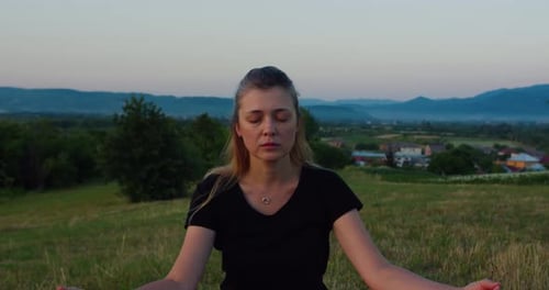 Close up shot of a woman practises yoga at sunrise on a meadow. Young spiritual girl meditates