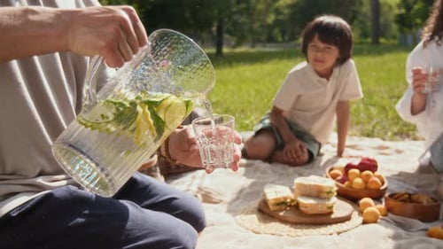 Close-up of Unrecognizable Man Poring Ice Lemonade for his Son During Picnic