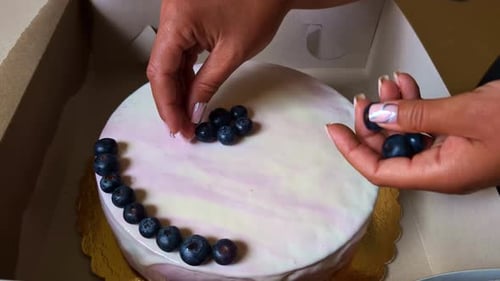 Womans hands are decorating a delicious cake in a box with blueberries, close up in slow motion