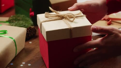 Hands Place Gift Among Christmas Presents on Wooden Table