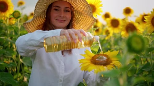 Woman Pours Sunflower Oil on a Sunflower Flower While Standing in a Field