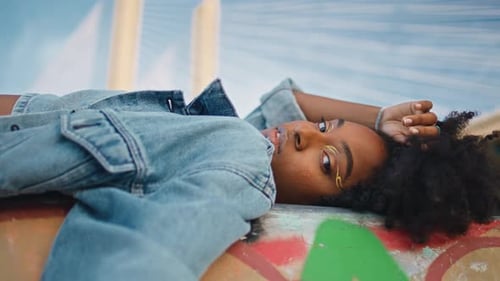 Elegante modelo posando acostada al aire libre con una chaqueta de jeans, niña de cerca relajándose