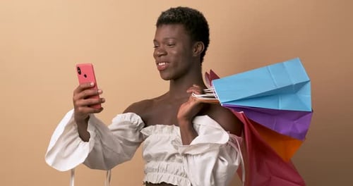Transgender African Person Using Phone and Holding Shopping Bags