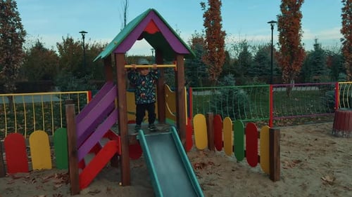 Energetic Caucasian toddler is on the playground. Happy cheerful kid is on the slide in autumn.