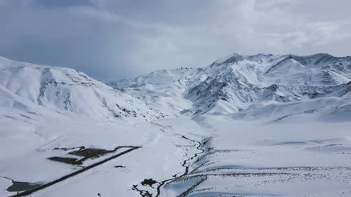 Aerial view drone flying over beautiful white snowy mountains landscape and a cloudy sky.