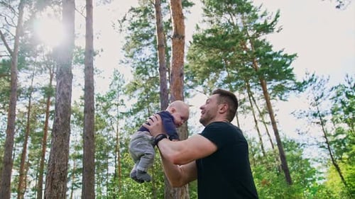 Handsome muscular Caucasian man tossing his little baby boy. Spending time with child in nature.