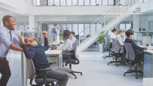 Un employé joyeux pousse son beau collègue sur une chaise à côté de rangées de bureaux avec des affaires diverses