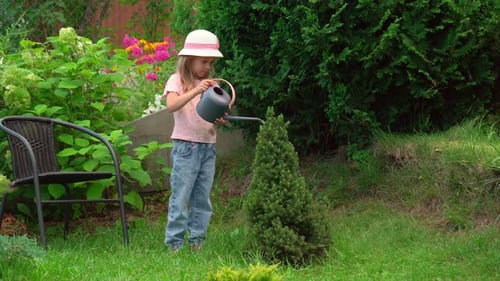 Little Girl Watering Plants From Watering Can in Summer Garden with Flowers