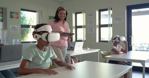 African teacher walking in class urging teenage female donning VR headset reaching exploring lesson