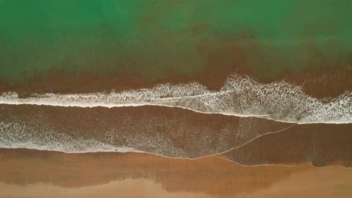 Top down perspective of ocean waves crashing on dark sandy beach in Costa Rica
