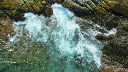An aerial shot of ocean waves crashing against rocks.