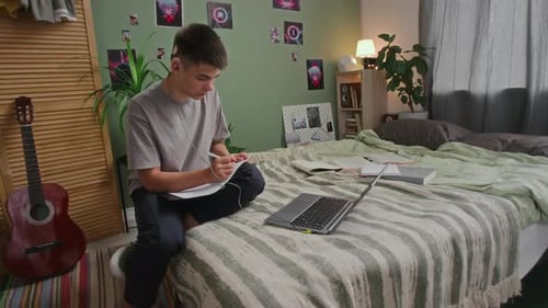 Jugendlicher mit Hörbehinderung hört Vorlesung auf dem Laptop und macht sich Notizen