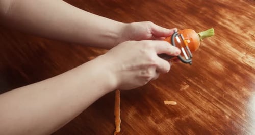 Primer plano de una persona pelando una zanahoria fresca con un pelador de verduras sobre una mesa de madera preparándose