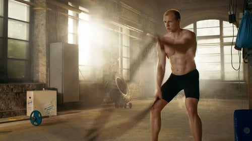 Muscular Shirtless Man in a Gym Exercises with Battle Ropes During Her Cross Fitness Workout High-
