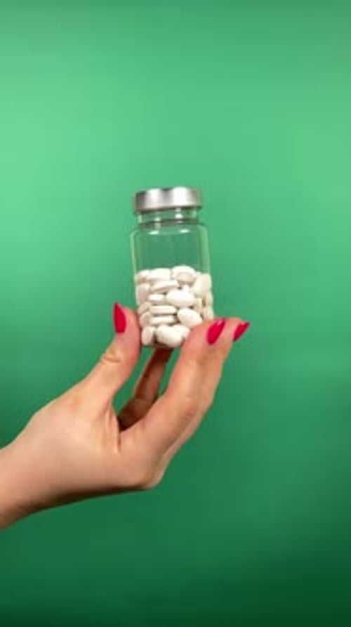 Hand Holding Pill Bottle Against Green Background