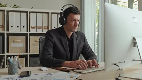 Empresario con auriculares trabajando en la computadora y haciendo papeleo